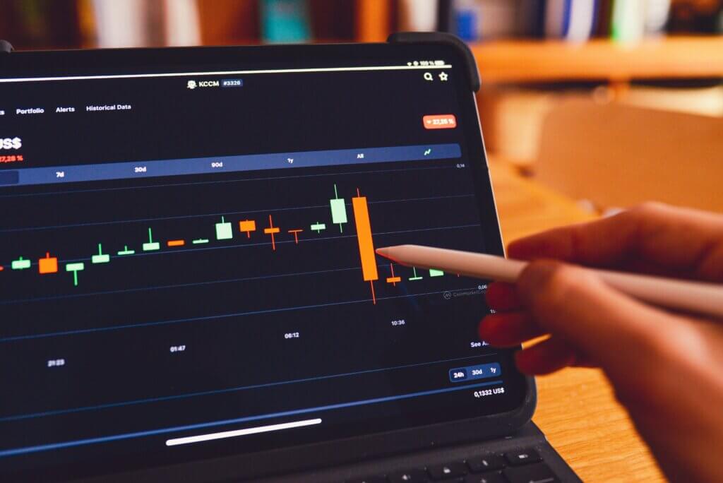 A trader pointing to a candlestick chart on their laptop screen